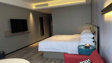 A modern hotel room with a bed, bedside table, TV, and a small round table.