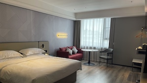 A hotel room with a large bed, a red sofa, a small round table, and a chair. - Borrman Hotel Foshan Nanhai Junya Plaza (Foshan)