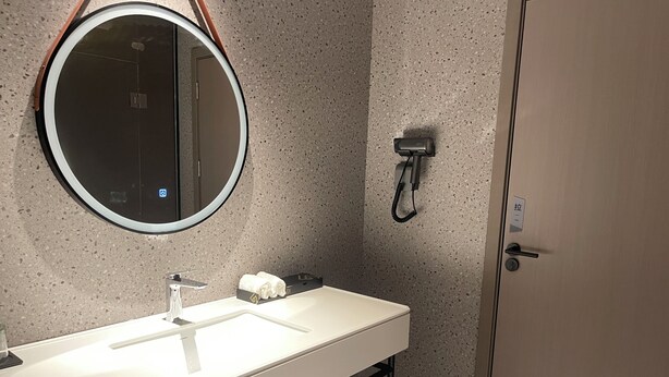 A bathroom with a round mirror, a sink, a towel rack, and a door. - Borrman Hotel Foshan Nanhai Junya Plaza (Foshan)