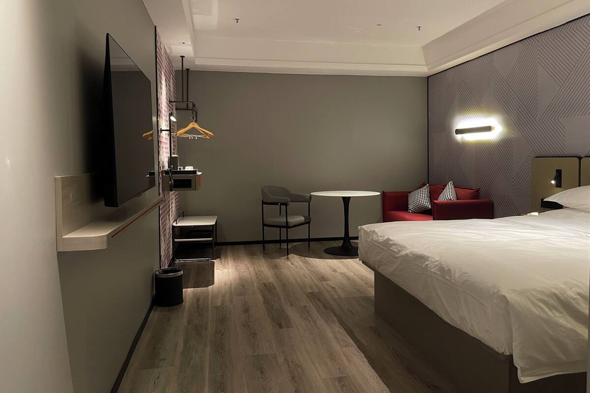 A hotel room with a bed, a small table, a chair, a TV, and a mirror.