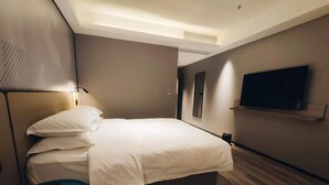 Une chambre d’hôtel avec un lit, une télévision, une petite table et une étagère fixée au mur.