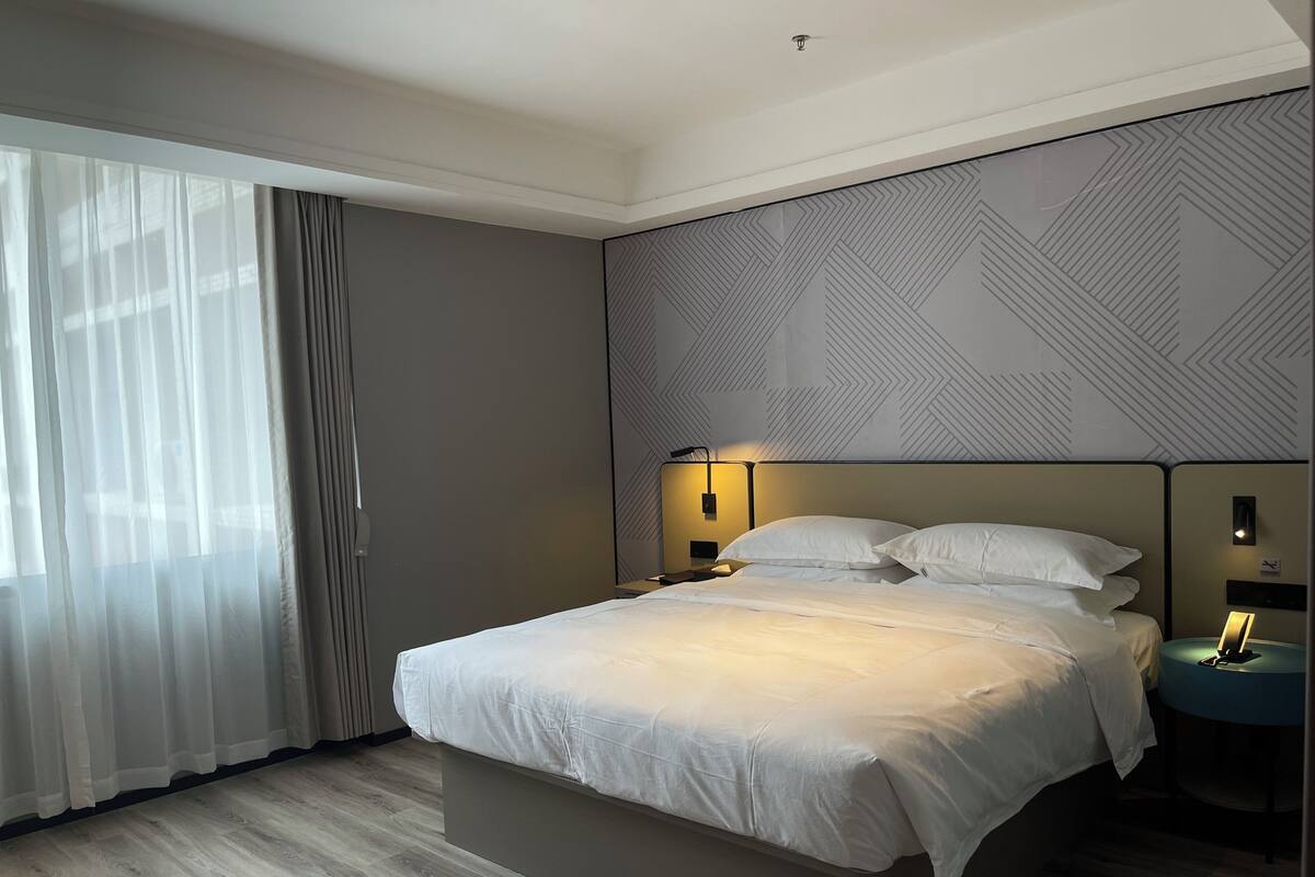 A modern hotel room with a large bed, a nightstand, a wall-mounted lamp, and a patterned wall.
