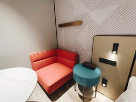 Una habitación de hotel moderna con un sofá rojo, una mesa redonda azul y un mueble beige con interruptor de luz.