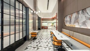 Un restaurant moderne, avec un intérieur élégant, un sol carrelé aux motifs géométriques, de longues tables conviviales et un grand panneau lumineux présentant le menu.
