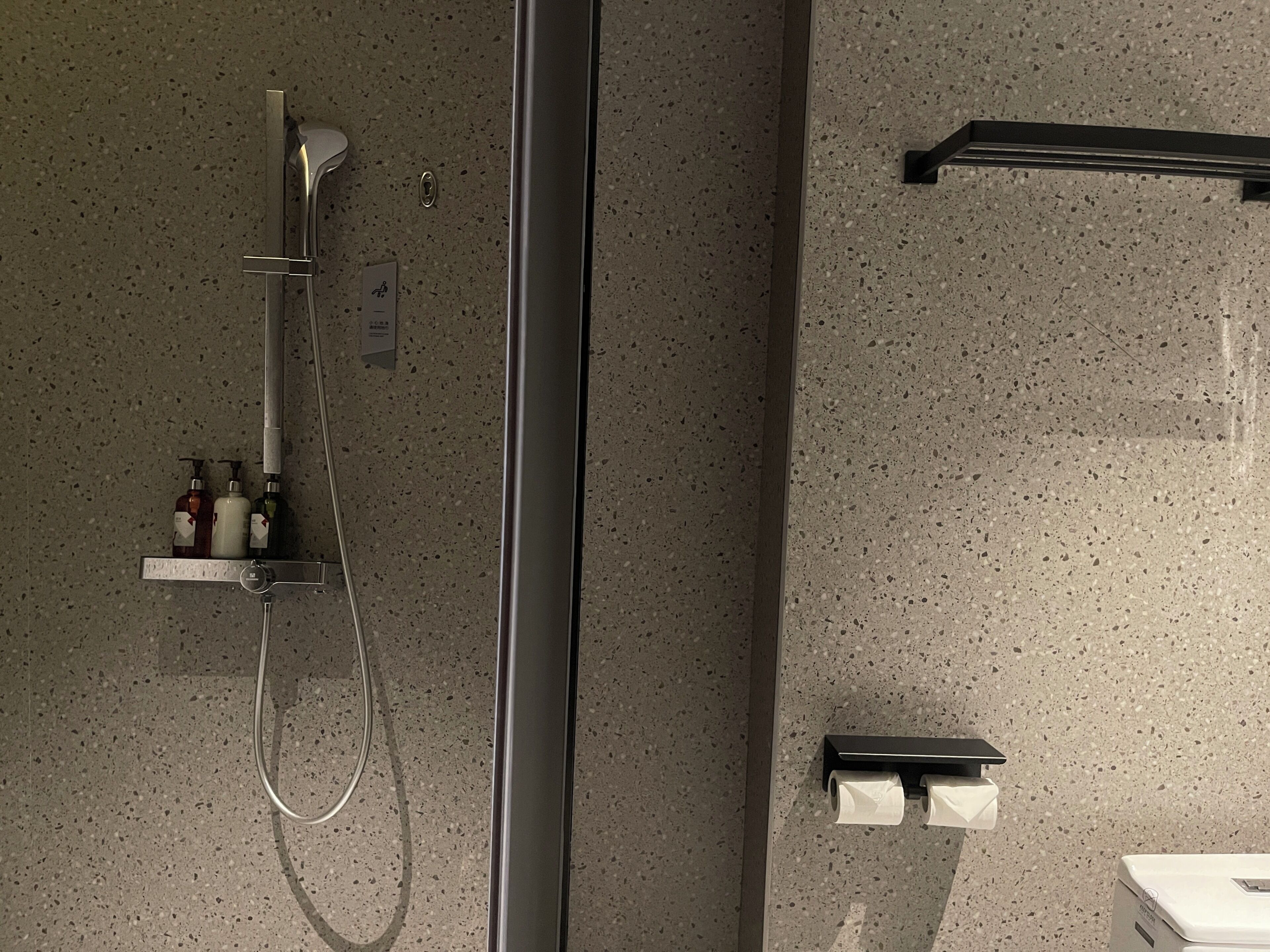Une salle de bain équipée d’une douche, de distributeurs de savon, d’un porte-serviettes et d’un support à papier toilette.