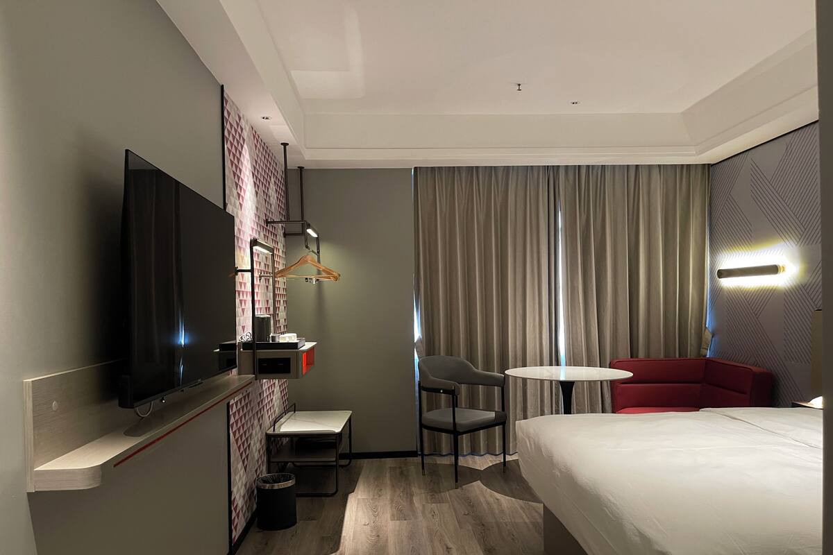A hotel room with a bed, a TV, a desk with a chair, a small table, and a sofa.