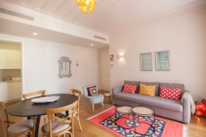 Ein Wohnzimmer mit einer Couch, Sesseln, einem Esstisch und einem gemusterten Teppich.