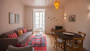 A living room with a sofa, a dining table with chairs, a TV, and a door leading outside. - FLH Restauradores Bright & Chic Flat with Balcony (Lisboa ciudad)