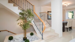 A modern staircase with a wooden handrail, a potted plant, and a dining area with a table and chairs.