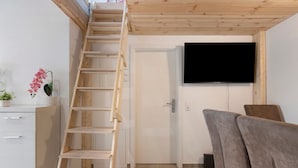Una stanza con una scala di legno, una porta bianca, una televisione a schermo piatto e un divano grigio.