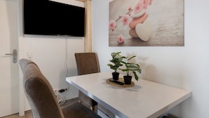 Una camera moderna con una TV a schermo piatto montata a parete, un tavolo da pranzo con due piante in vaso e un quadro con fiori.