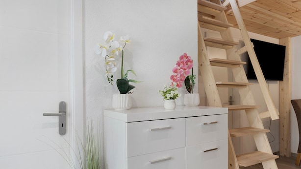 Un mobile bianco con cassetti, una scala in legno e orchidee in vaso.