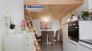 Una cucina moderna con mobili bianchi, soffitto in legno e zona pranzo con due sedie e un tavolo.