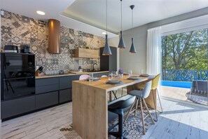 A modern kitchen with a wooden island, pendant lights, and a view of the outdoors. - Ultra-modern vacation home for 6 with swimming pool in Crikvenica (Crikvenica)