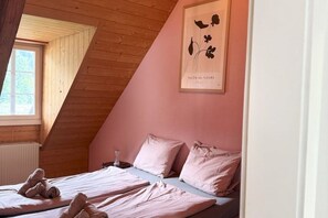 A bedroom with a sloped ceiling, a bed with pink bedding, a bedside table, and a framed floral artwork on the wall.