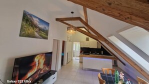 Un loft spacieux avec un plafond haut, un coin cuisine, une table à manger et un grand téléviseur à écran plat.