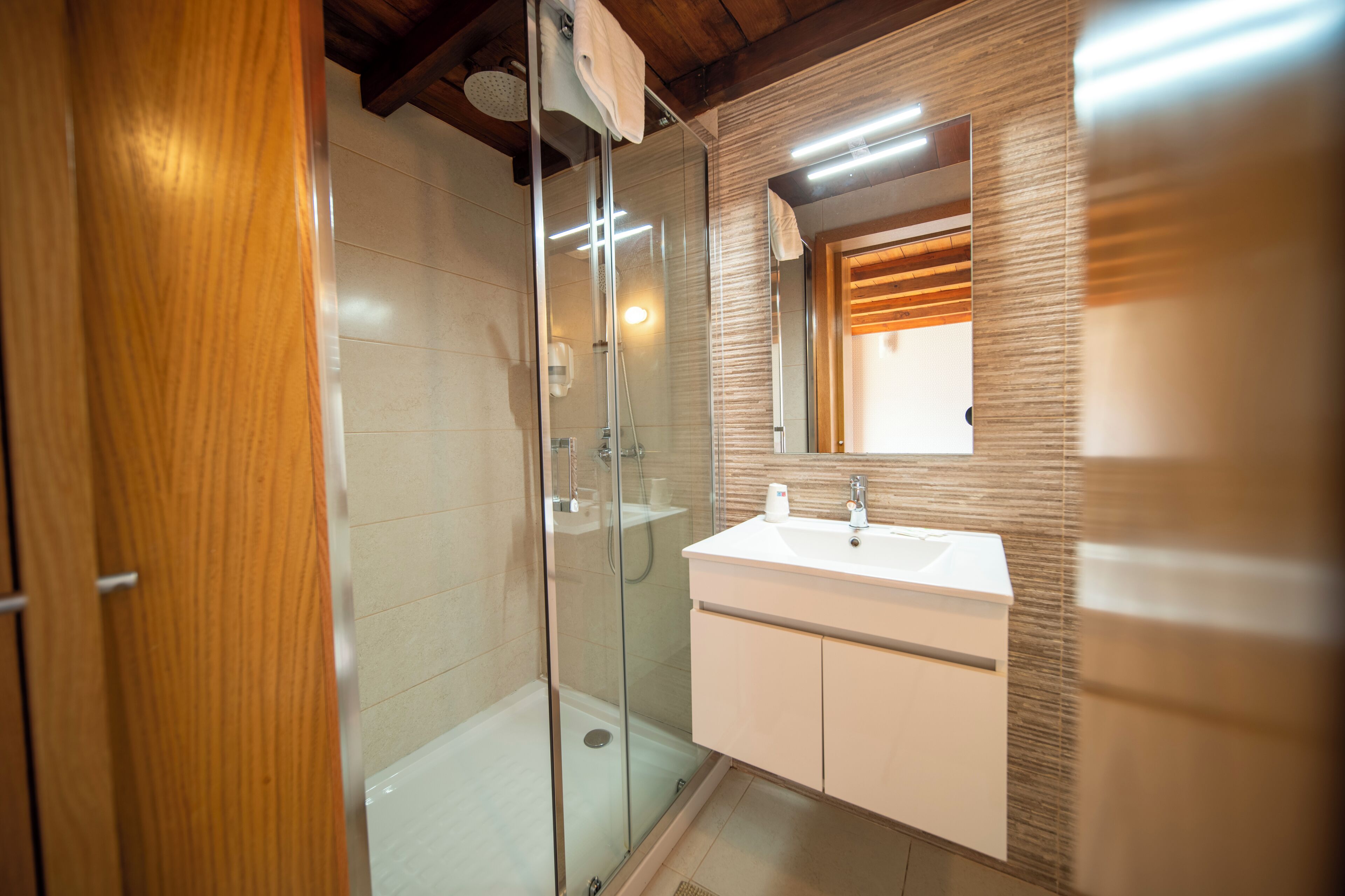 Ein modernes Badezimmer mit Duschkabine aus Glas, einem weißen Waschbecken und einem Holz-Waschtisch.