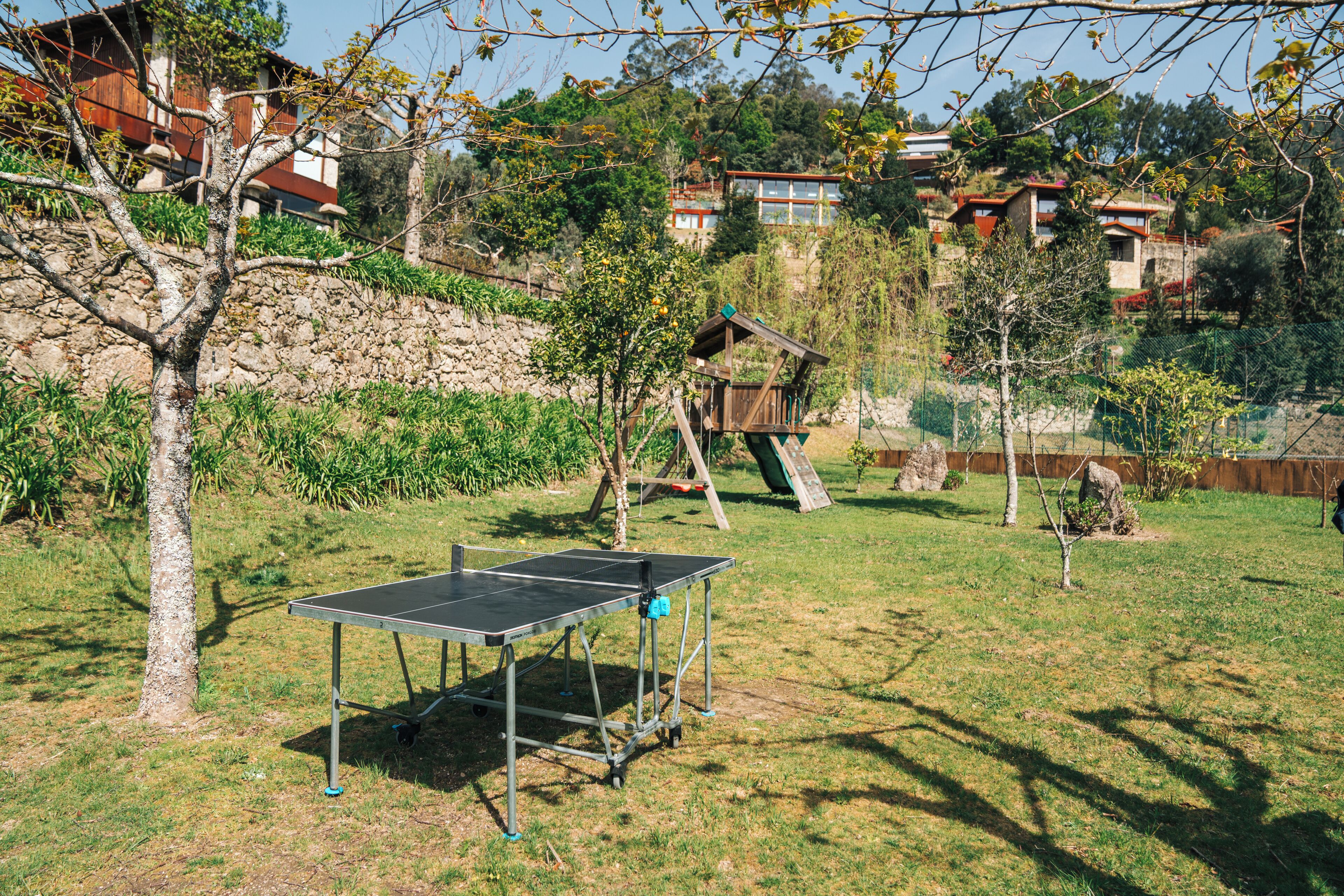 A ping pong table in a grassy area with trees and a playground in the background.