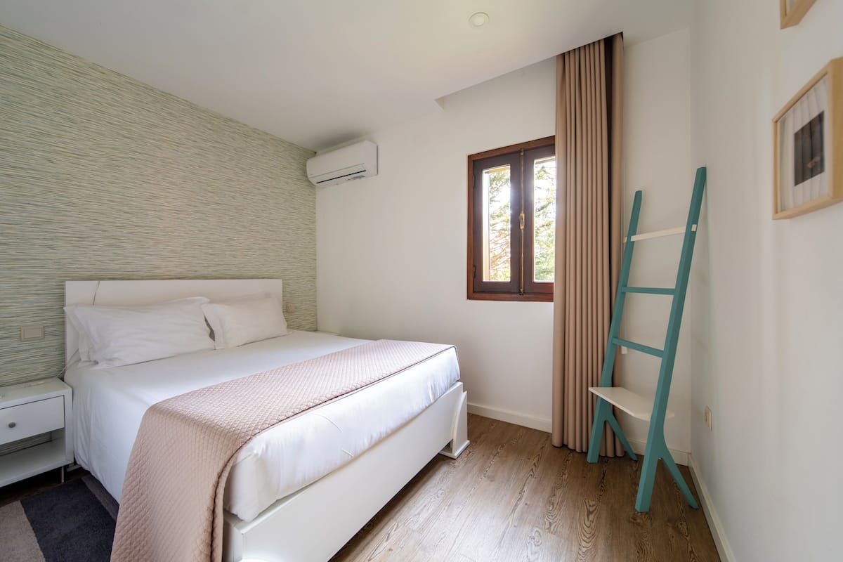 Une chambre à coucher avec un lit, une fenêtre avec des rideaux, une échelle et un appareil de climatisation.