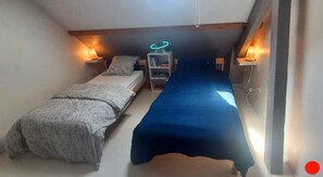 A small room with two beds, a bookshelf, and two wall-mounted lamps.