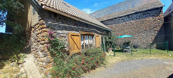 A stone building with a wooden door, a gravel path, and a blue umbrella.