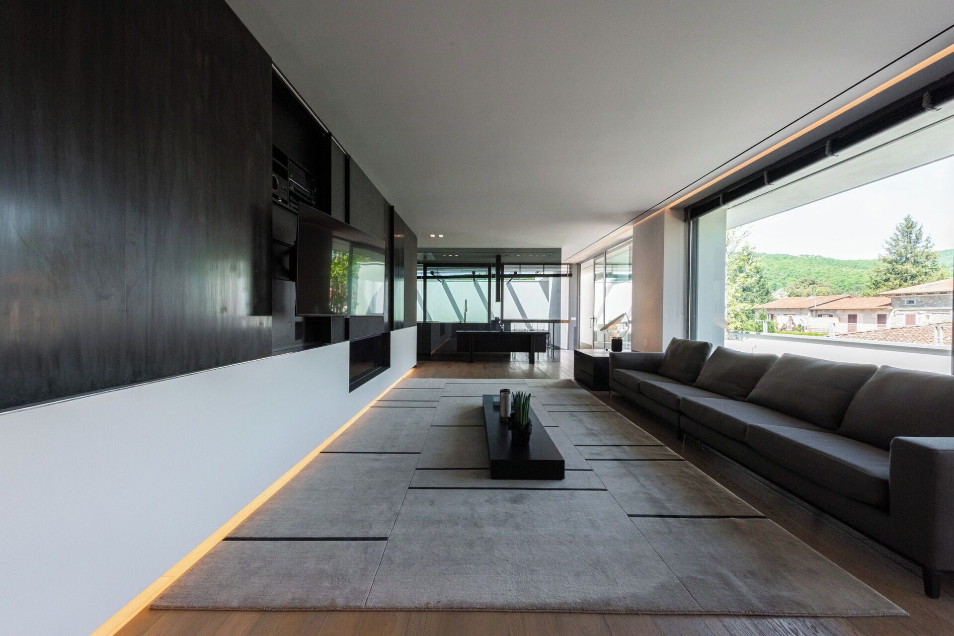 A modern interior with a sofa, a coffee table, and a kitchen area visible through a glass wall.