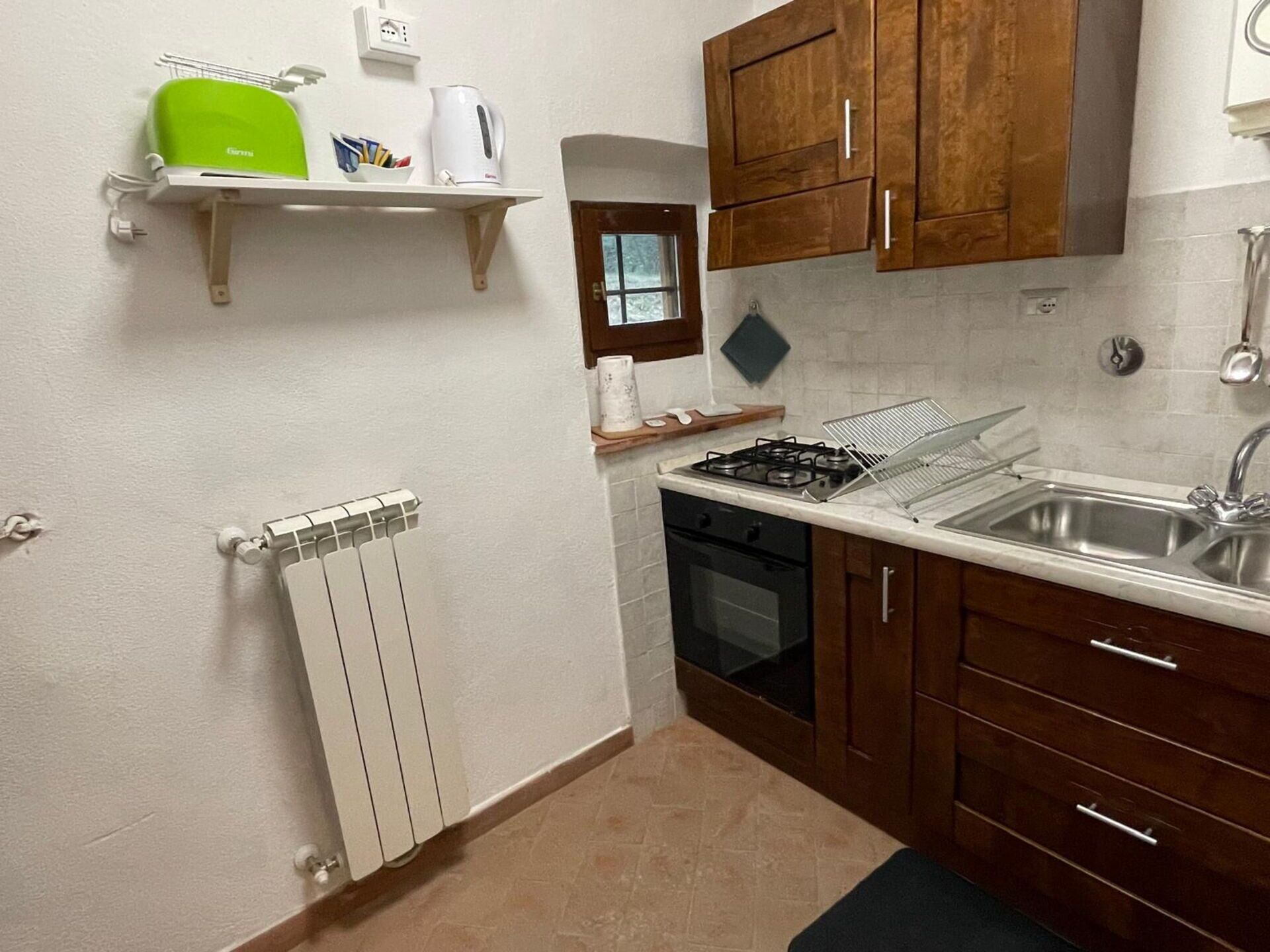 A compact kitchen with a gas stove, a sink, wooden cabinets, a white countertop, and a small window.