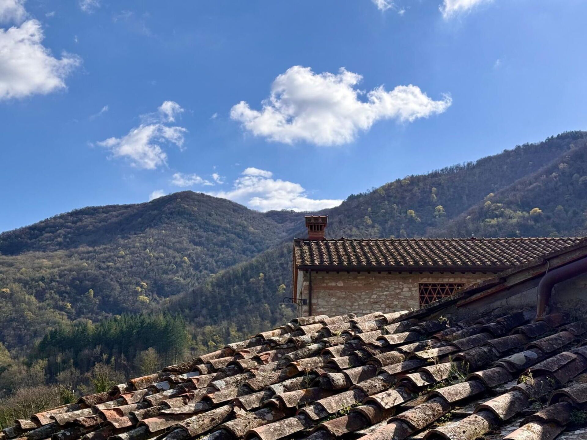 A rustic stone building with a tiled roof, surrounded by a mountainous landscape.