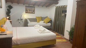 Un dormitorio con cama, sofá, escritorio con lámpara, un cuadro y ventana con cortinas.