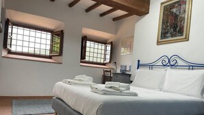 Un dormitorio con una cama, dos ventanas, un cuadro y un escritorio.