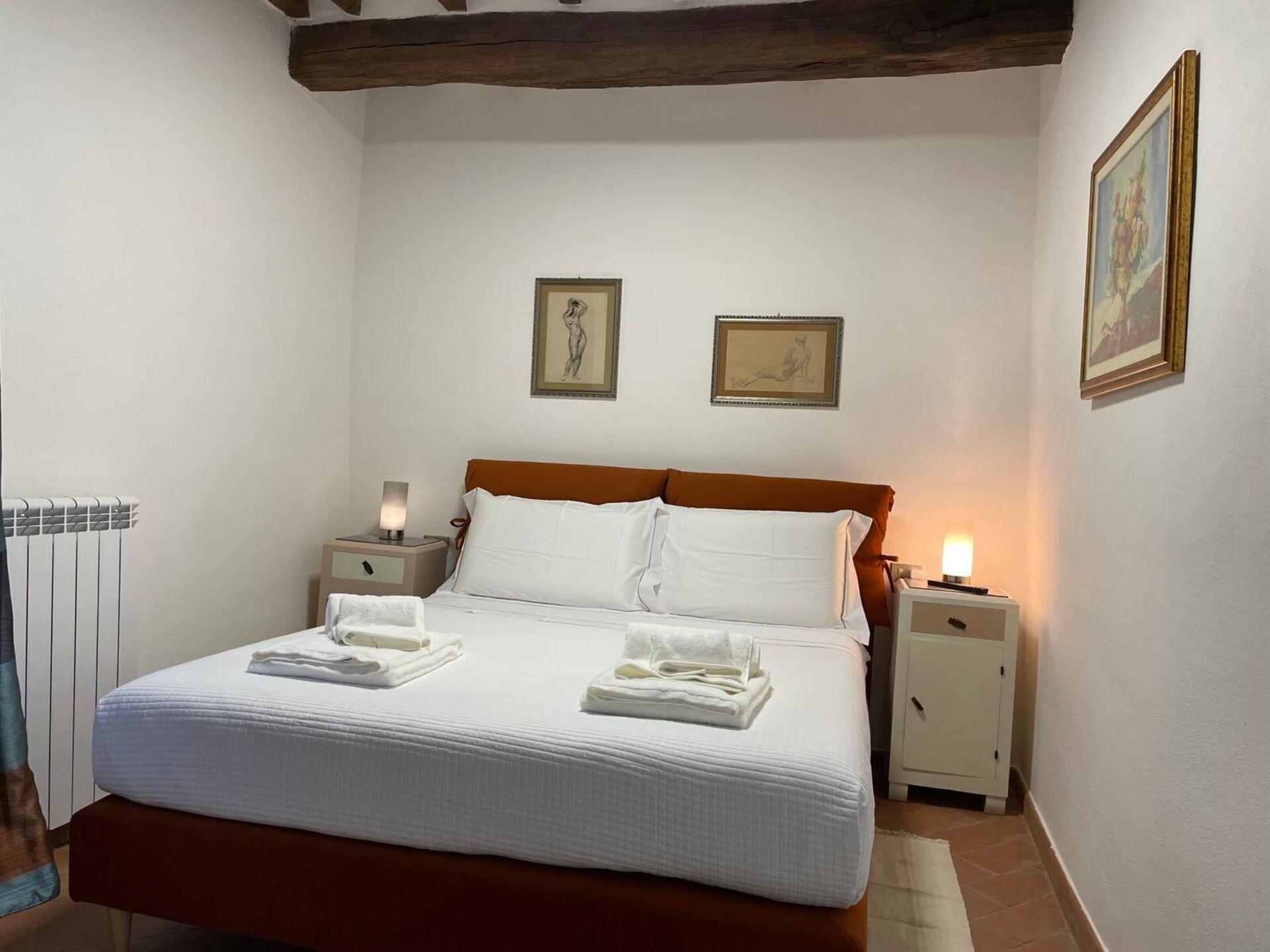 A neatly made bed with white linens and pillows, two bedside tables with lamps, and two framed artworks on the wall.