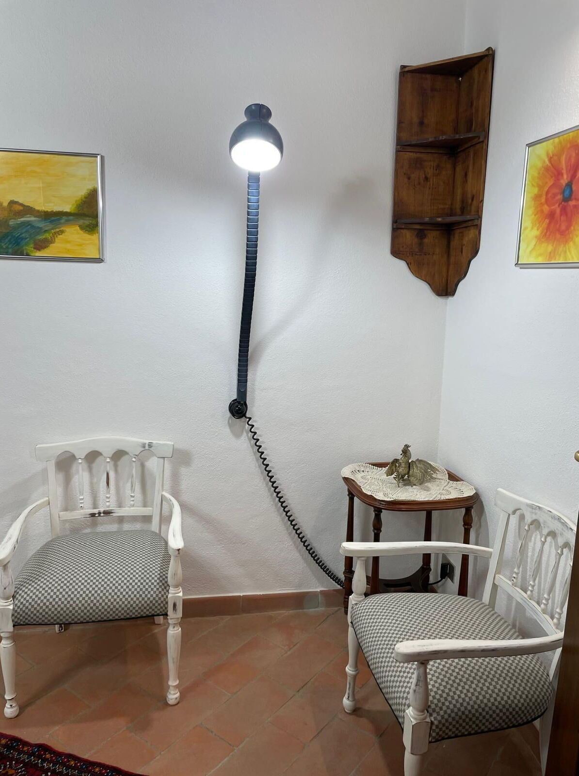 A room with two white chairs, a small table with a decorative item, a wall-mounted shelf, and a ceiling lamp.