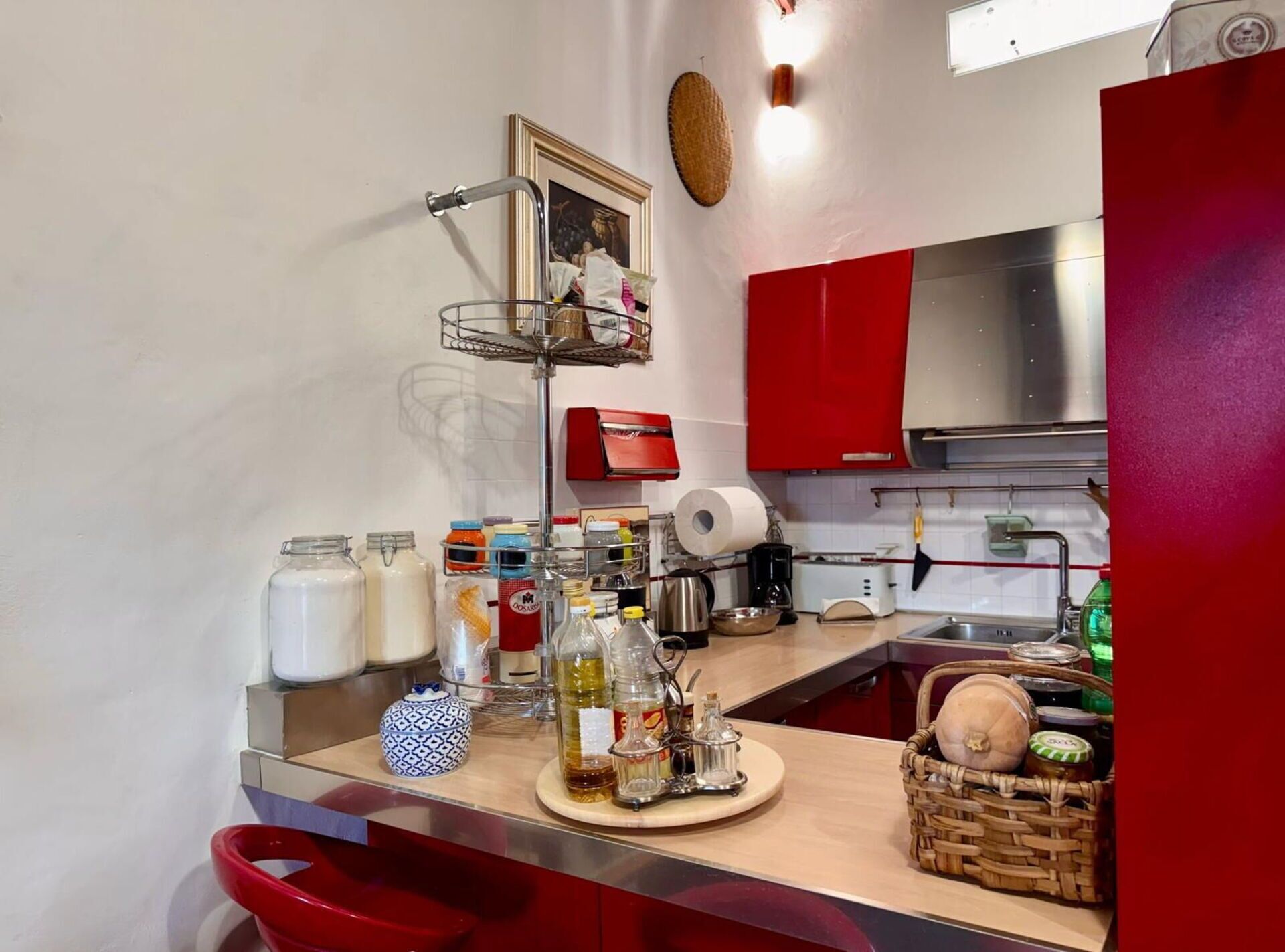 A kitchen with a metal rack holding jars, a coffee maker, and a basket with a round object.