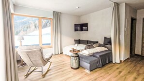 Une chambre à coucher avec un lit, une chaise, une télévision et une fenêtre avec des rideaux.