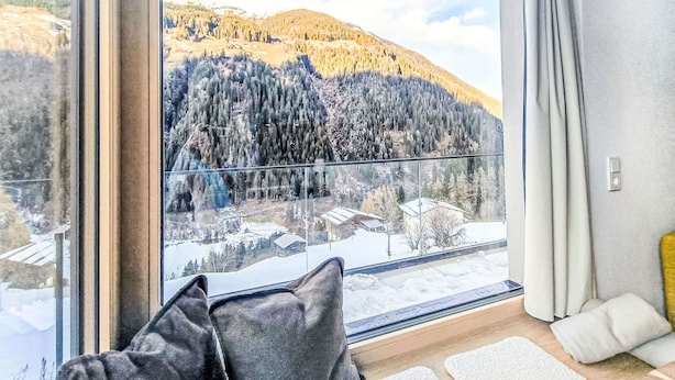 Quarto com uma grande janela, vista para montanhas cobertas de neve e guarda-corpo de vidro.