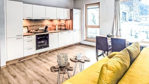 Cozinha moderna com armários brancos, área de jantar com sofá amarelo e vista para o horizonte urbano pela janela.