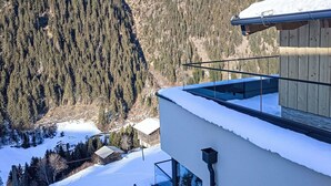 Um edifício moderno com varanda de vidro que oferece vista para uma paisagem montanhosa coberta de neve.