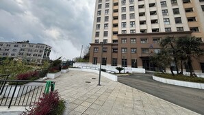 Un edificio de varios pisos con techo plano, entrada protegida por una reja y un patio empedrado con plantas.