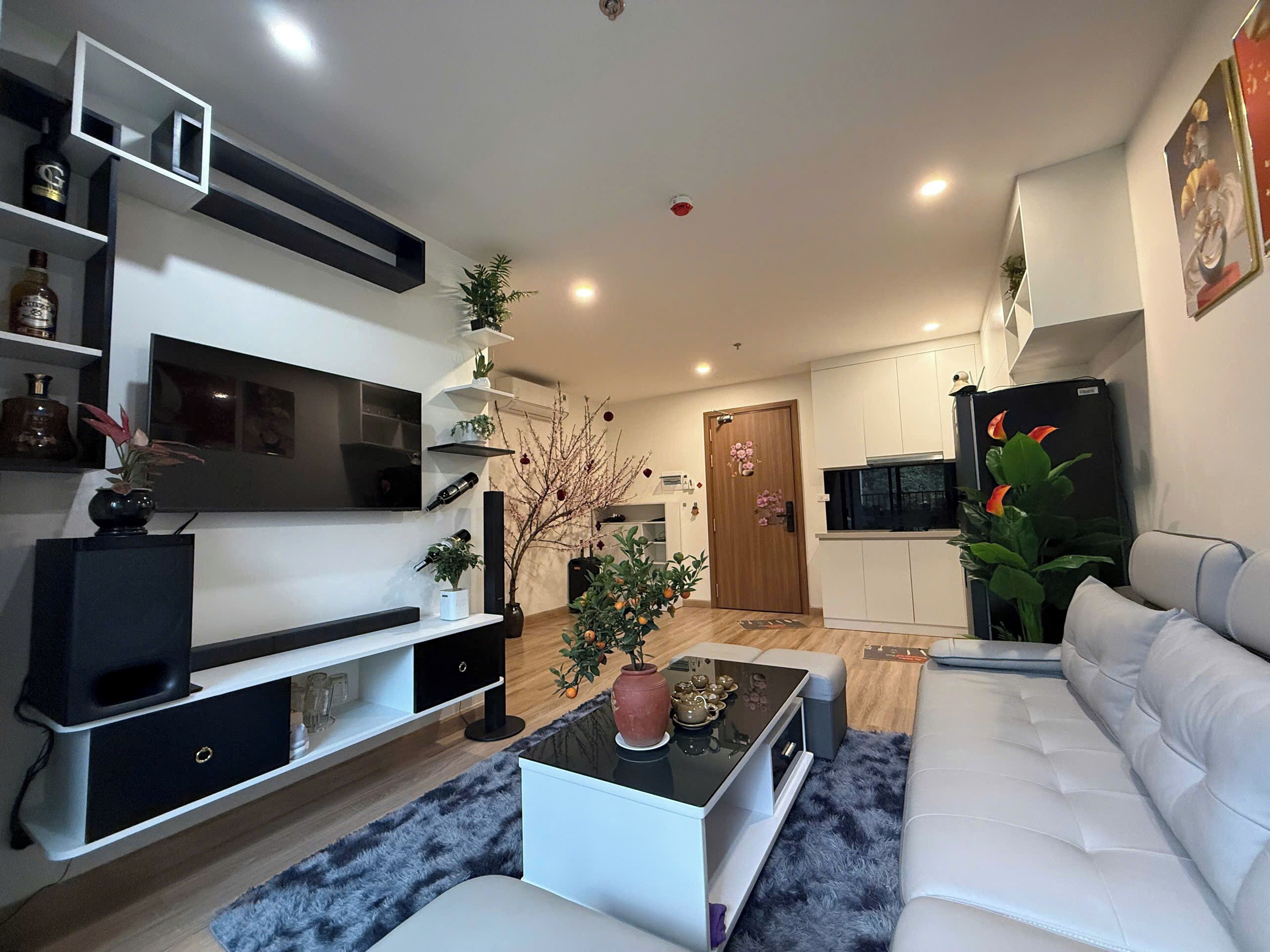 Un saló modern amb un sofà, una taula de centre, televisió i zona de cuina amb nevera i armaris.