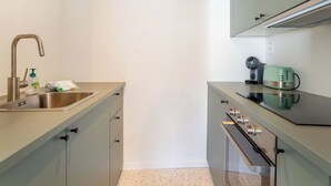 Una kitchenette compacta con un lavamanos de acero inoxidable, una cafetera, un tostador y un microondas.