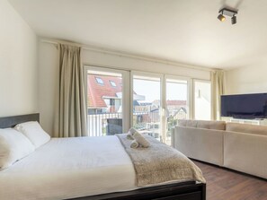 Ein Hotelzimmer mit Bett, Sofa, Fernseher und großen Fenstern mit Blick auf Gebäude.