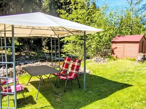 Un espacio de estar al aire libre techado con una mesa, sillas, un cobertizo pequeño y un patio cubierto de césped.
