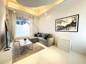 Ein modernes Wohnzimmer mit Ecksofa, Couchtisch, Flachbildfernseher, gerahmtem Kunstwerk und einer weißen Kommode.