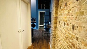 Un couloir au sol en bois, avec un mur de briques d’un côté et une porte blanche de l’autre.