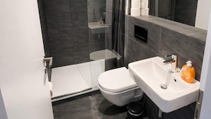 Une salle de bain moderne avec une douche à parois de verre, des toilettes blanches, un lavabo avec un miroir et une poubelle.