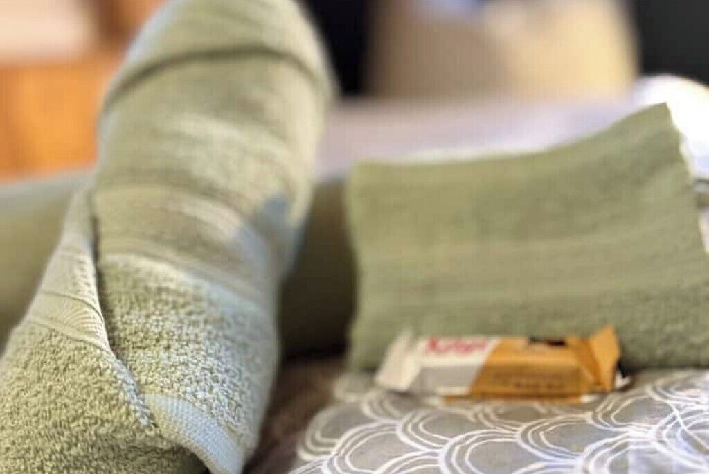 Detailaufnahme eines grünen Stoffes, möglicherweise ein Handtuch oder eine Decke, mit einem kleinen Gegenstand auf einem Kissen.