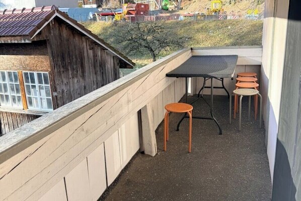 A balcony with a table and stools, a wooden fence, and a view of a rural landscape.