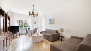 Ein Wohnzimmer mit einer Couch, einem Fernseher, einem Esstisch und einer Pendelleuchte.