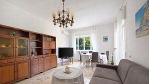 Ein Wohnzimmer mit einer Couch, einem Fernseher, einem Esstisch und einer Chandelier.