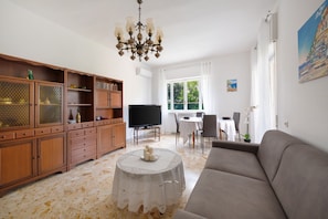 A living room with a sofa, a television, a dining table, and a chandelier. - Holiday Home 'Casa Mamma Margherita' with Mountain View, Wi-Fi and Air Conditioning (Sorrento)